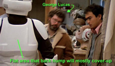 screencap from the Making Magic Archive CD which highlights behind the scenes image of a Biker Scout costume being fitted and reviewed by George Lucas. This image clearly shows the back of the scout costume without the back hump attached. You can clearly see teh flat panel that gets covered by the back hump
